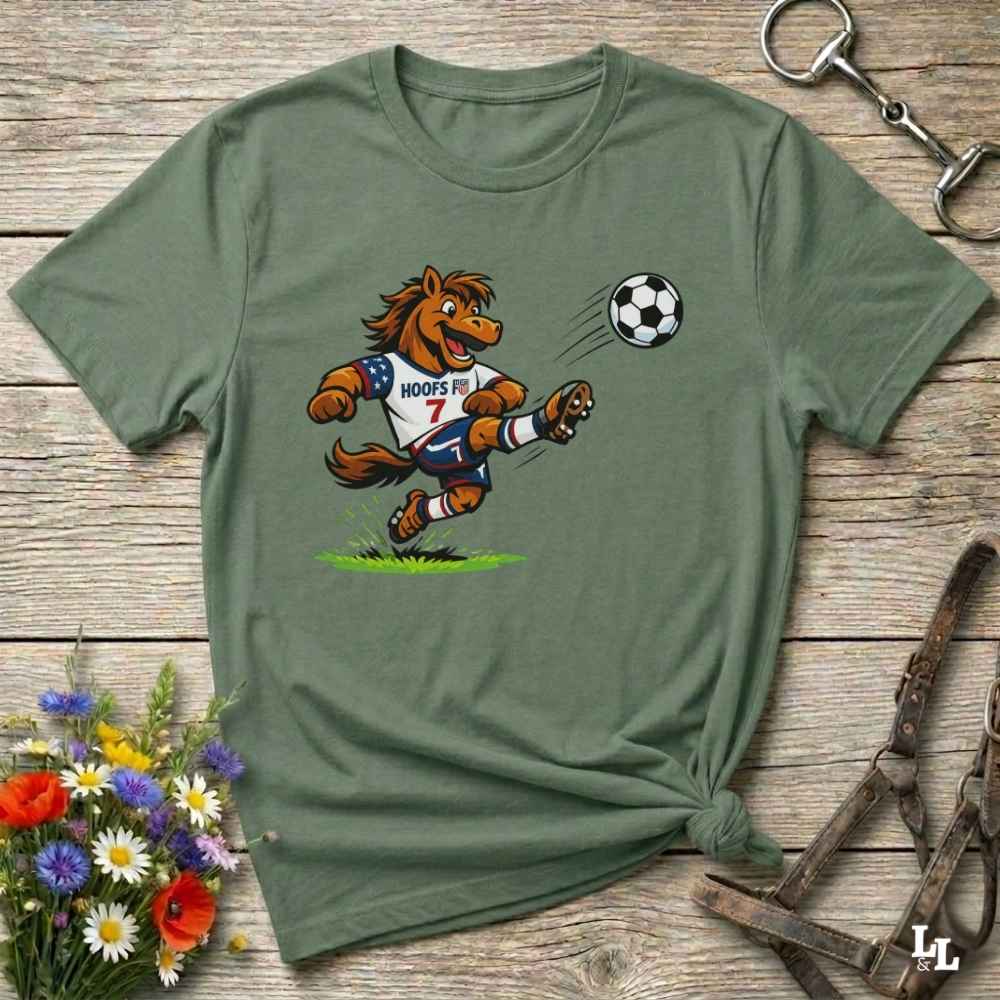 green t-shirt with a cartoon horse kicking a soccer ball on a wooden surface with flowers and horse halter and bit.