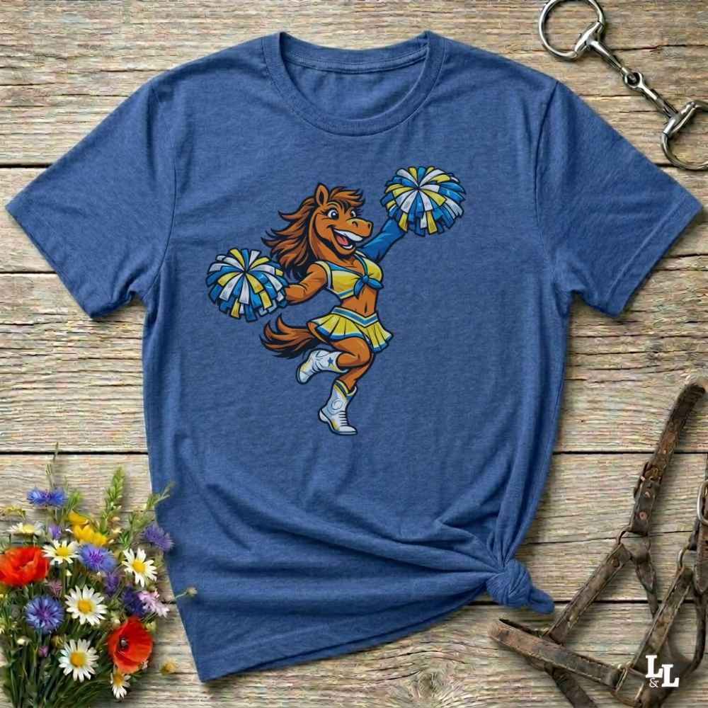 Blue t-shirt with a cartoon horse cheerleader design on a wooden surface with flowers and a horse bit