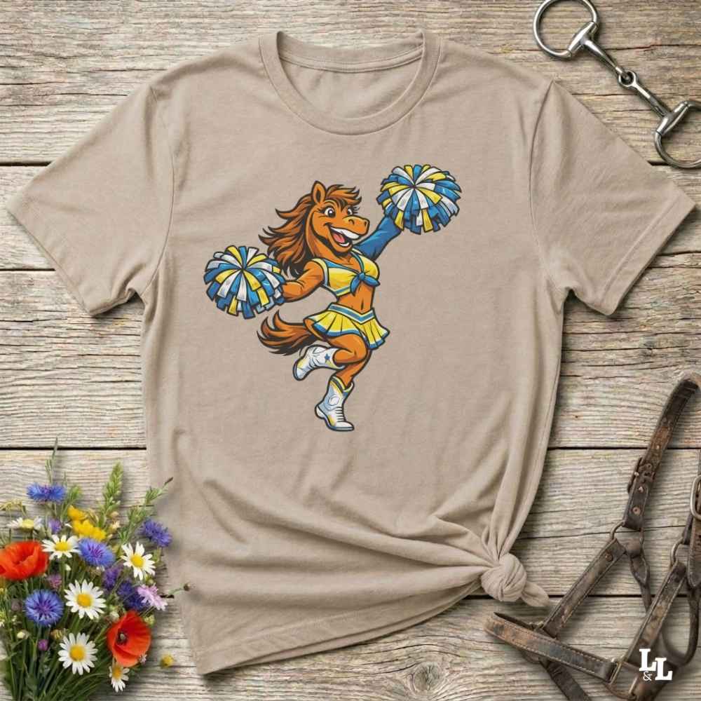 beige  t-shirt with a cartoon horse cheerleader design on a wooden surface with flowers and a horse bit