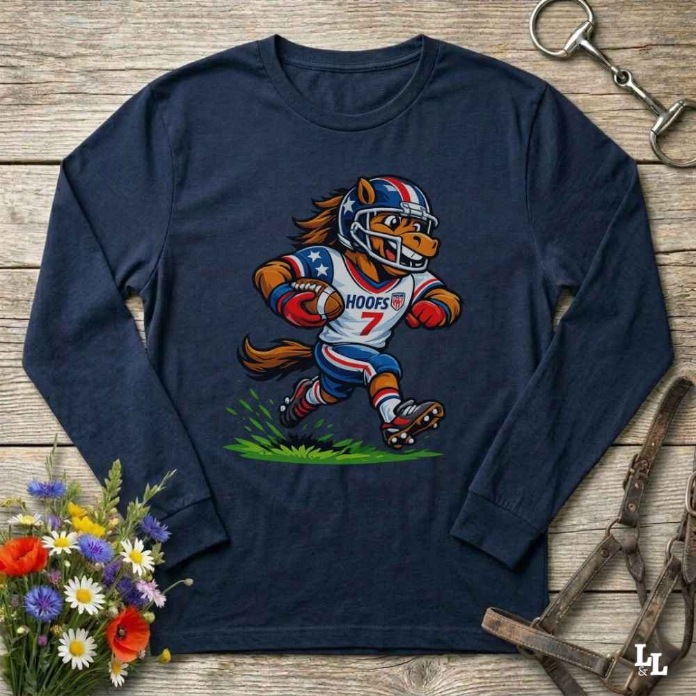 A navy blue long-sleeve t-shirt with a cartoon graphic of a horse running as a football player wearing a red, white, and blue helmet. The shirt is displayed flat on a rustic wooden background with decorative flowers and horse tack.