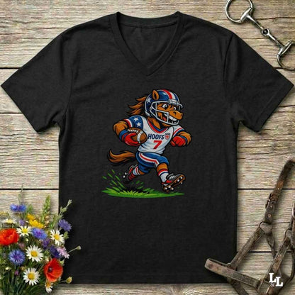 A black V-neck t-shirt laid flat on a rustic wooden surface, featuring a cartoon graphic of a horse mascot in a football uniform with the number 7. The shirt is styled with equestrian tack in the background and a small bouquet of flowers in the lower-left corner.