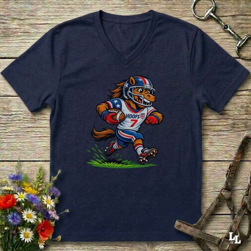 A blue  V-neck t-shirt laid flat on a rustic wooden surface, featuring a cartoon graphic of a horse mascot in a football uniform with the number 7. The shirt is styled with equestrian tack in the background and a small bouquet of flowers in the lower-left corner.