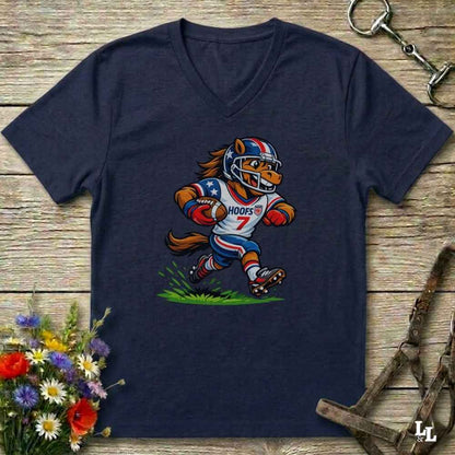 A blue  V-neck t-shirt laid flat on a rustic wooden surface, featuring a cartoon graphic of a horse mascot in a football uniform with the number 7. The shirt is styled with equestrian tack in the background and a small bouquet of flowers in the lower-left corner.
