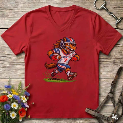 A red V-neck t-shirt laid flat on a rustic wooden surface, featuring a cartoon graphic of a horse mascot in a football uniform with the number 7. The shirt is styled with equestrian tack in the background and a small bouquet of flowers in the lower-left corner.