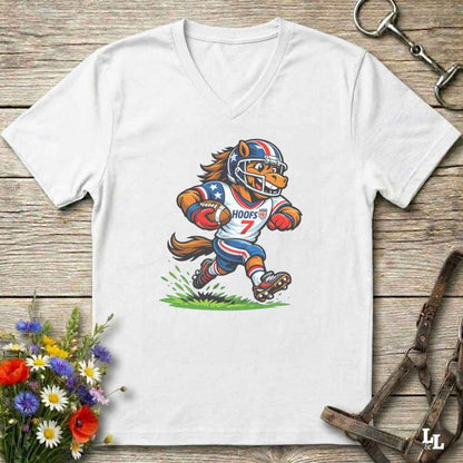 A white V-neck t-shirt laid flat on a rustic wooden surface, featuring a cartoon graphic of a horse mascot in a football uniform with the number 7. The shirt is styled with equestrian tack in the background and a small bouquet of flowers in the lower-left corner.