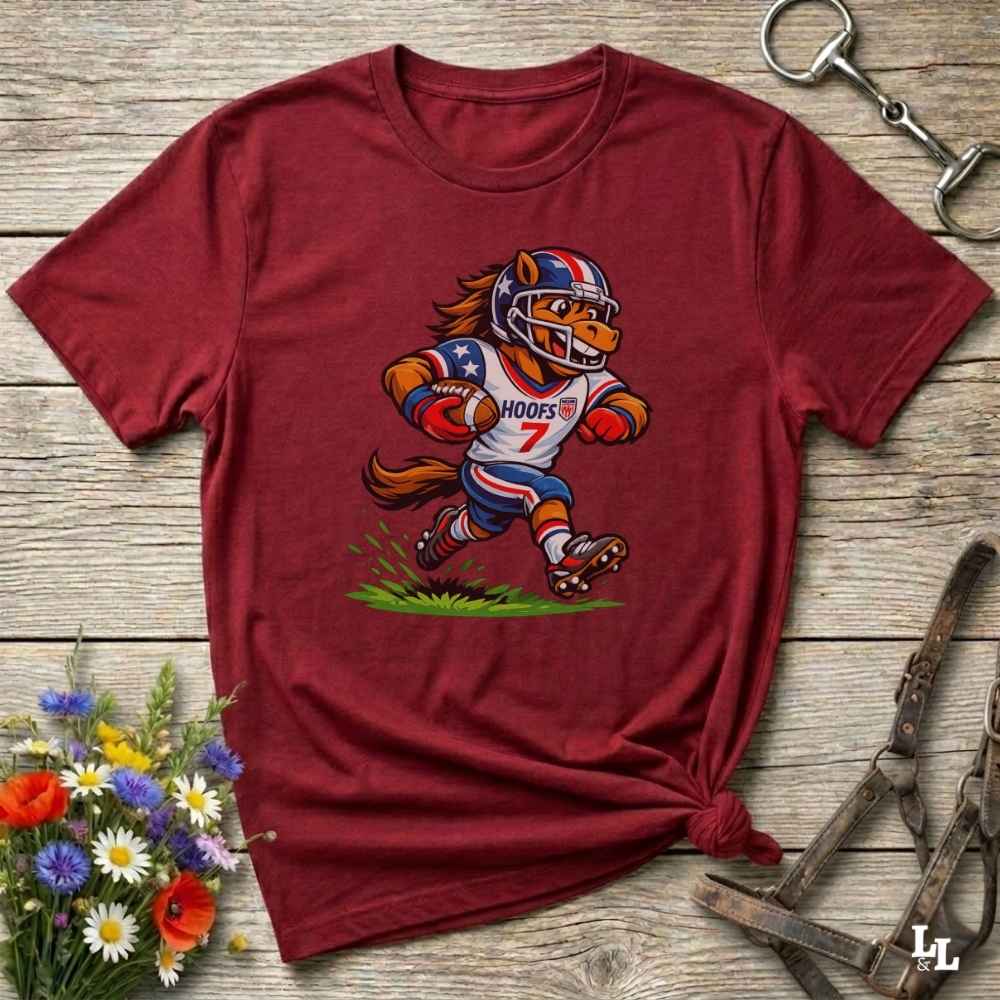 Maroon t-shirt with a cartoon football player design on a wooden surface with flowers and tools.