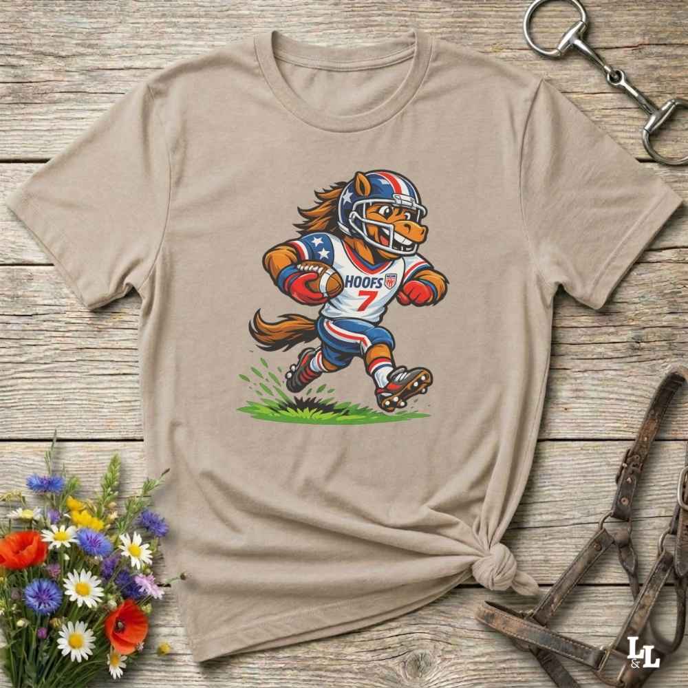 Beige t-shirt with a cartoon horse football player design on a wooden surface with flowers and tools.