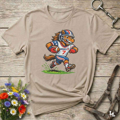 Beige t-shirt with a cartoon horse football player design on a wooden surface with flowers and tools.