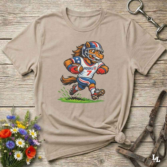 Beige t-shirt with a cartoon horse football player design on a wooden surface with flowers and tools.