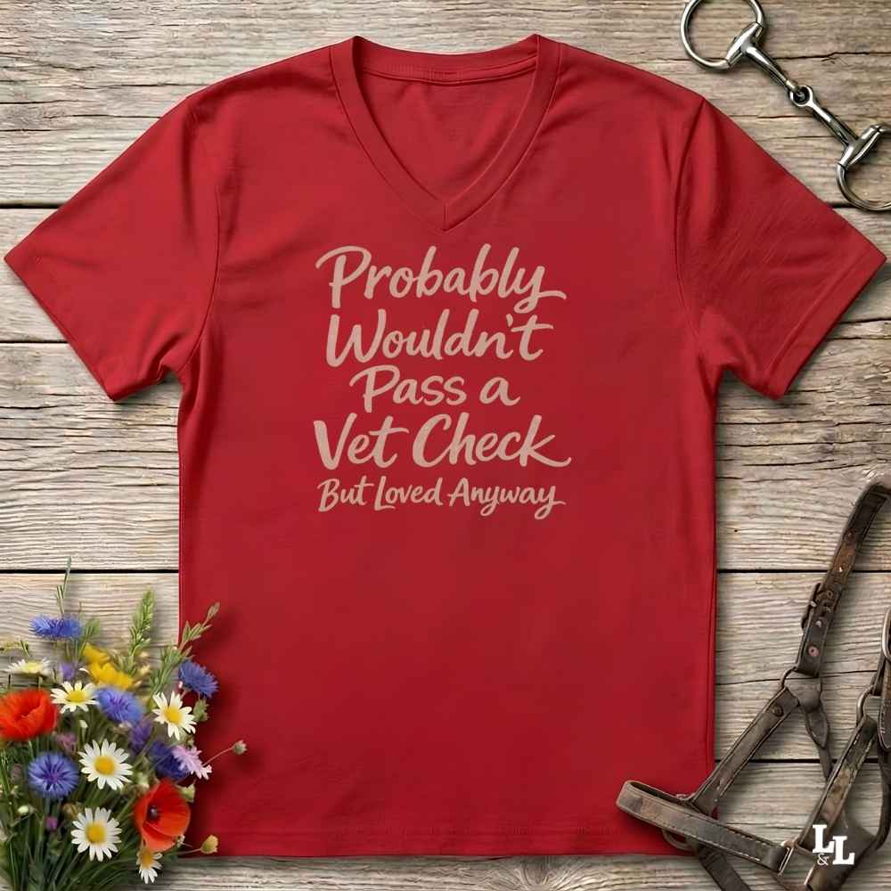 red v-neck t-shirt, with text "Probably Wouldn't Pass a Vet Check, bu tloved anyway". T-shirt lying on barn wooden floorboards, with flowers, horse halter and horse bit.