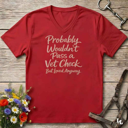 red v-neck t-shirt, with text "Probably Wouldn't Pass a Vet Check, bu tloved anyway". T-shirt lying on barn wooden floorboards, with flowers, horse halter and horse bit.