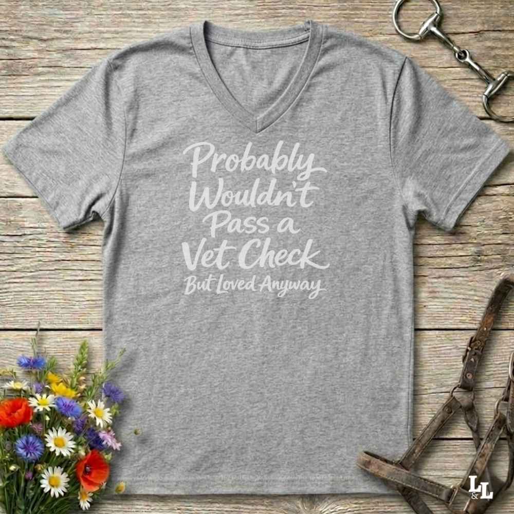 grey v-neck t-shirt, with text "Probably Wouldn't Pass a Vet Check, bu tloved anyway". T-shirt lying on barn wooden floorboards, with flowers, horse halter and horse bit.