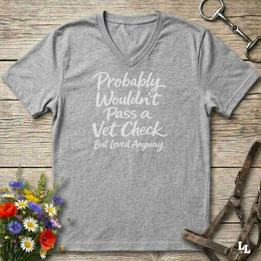 grey v-neck t-shirt, with text "Probably Wouldn't Pass a Vet Check, bu tloved anyway". T-shirt lying on barn wooden floorboards, with flowers, horse halter and horse bit.