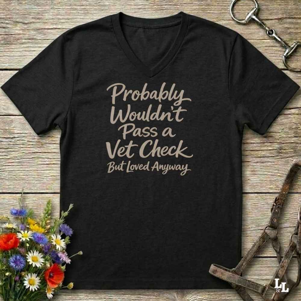 black v-neck t-shirt, with text "Probably Wouldn't Pass a Vet Check, bu tloved anyway". T-shirt lying on barn wooden floorboards, with flowers, horse halter and horse bit.