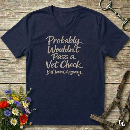 navy v-neck t-shirt, with text "Probably Wouldn't Pass a Vet Check, bu tloved anyway". T-shirt lying on barn wooden floorboards, with flowers, horse halter and horse bit.
