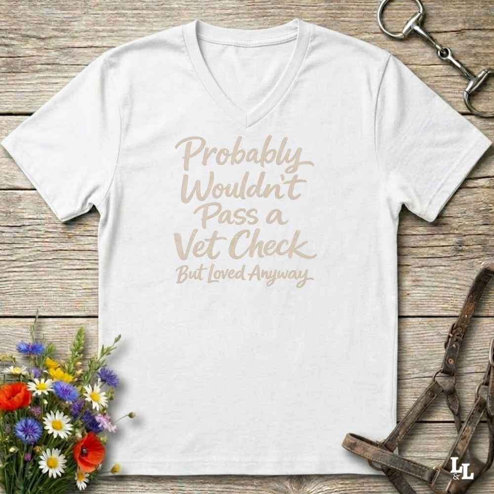 white v-neck t-shirt, with text "Probably Wouldn't Pass a Vet Check, bu tloved anyway". T-shirt lying on barn wooden floorboards, with flowers, horse halter and horse bit.