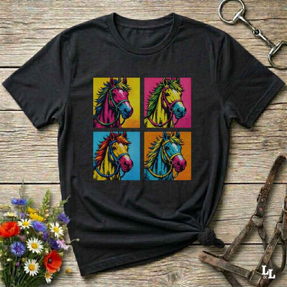 A black short-sleeve t-shirt with a colorful graphic print of four pop-art horses in a 2x2 grid, styled on a rustic wooden background with equestrian accessories and flowers.