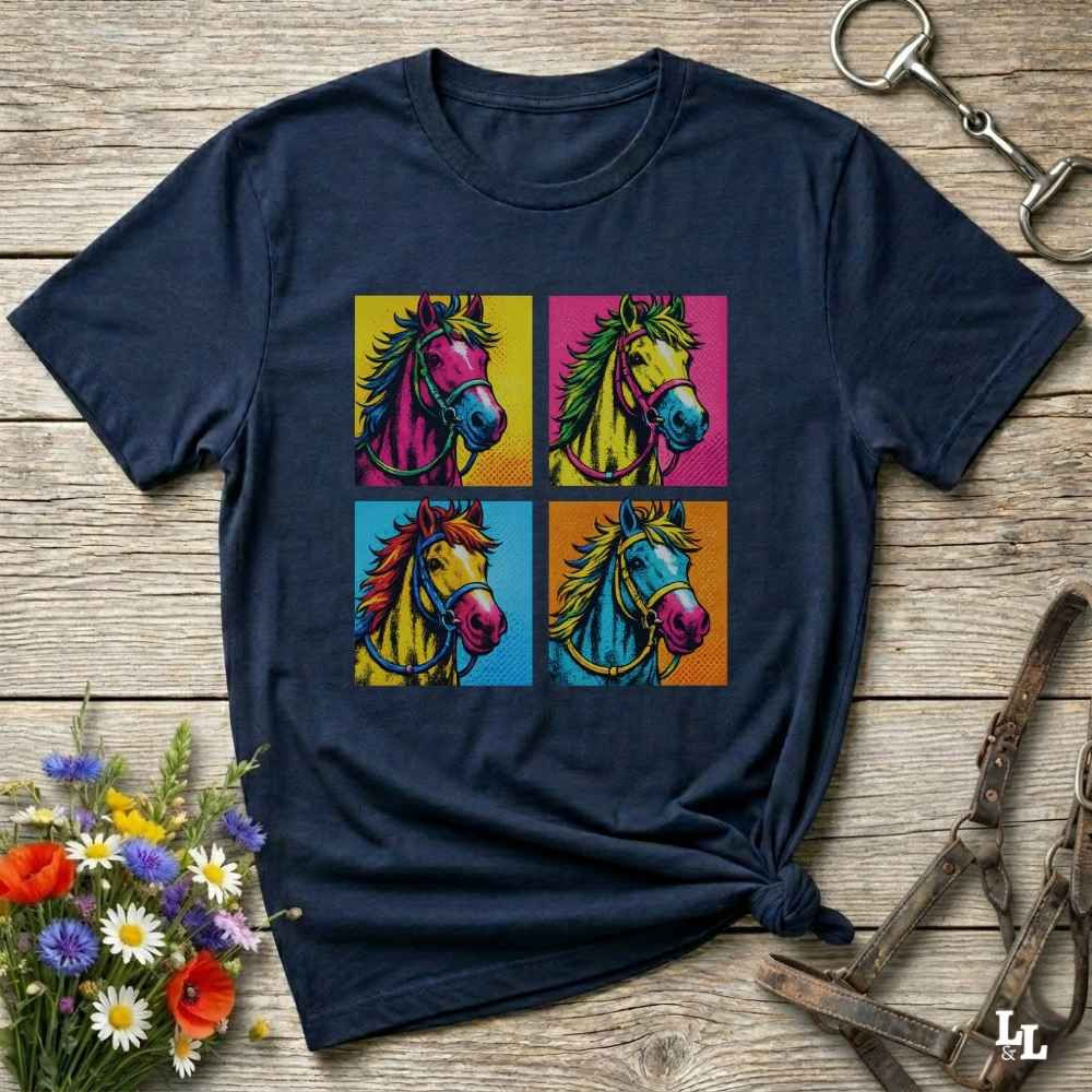 A navy blue short-sleeve t-shirt with a colorful pop-art graphic of four horses in a 2x2 grid, styled on a rustic wooden background with equestrian accessories and flowers.