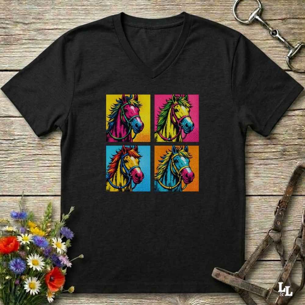 A black V-neck t-shirt featuring a colorful graphic print of four pop-art horse heads in yellow, pink, blue, and orange squares, displayed on a rustic wooden background with equestrian accessories and flowers.