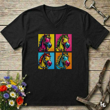 A black V-neck t-shirt featuring a colorful graphic print of four pop-art horse heads in yellow, pink, blue, and orange squares, displayed on a rustic wooden background with equestrian accessories and flowers.