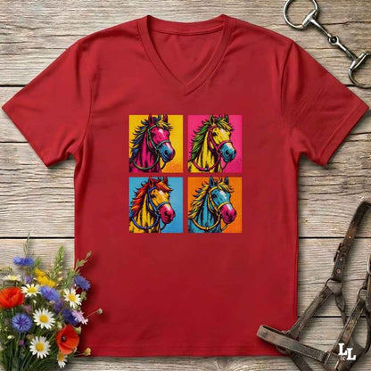 A red V-neck t-shirt laid flat on a rustic wooden surface, featuring a colorful pop-art graphic of four horse heads in a 2x2 grid. The shirt is styled with equestrian-themed props, including a horse bit in the top right, a halter in the bottom right, and a small bouquet of wildflowers in the bottom left.