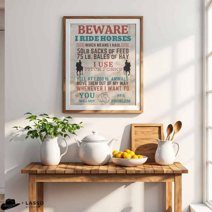 Framed humorous poster on a wall above a wooden table with kitchen.  Western Sign.