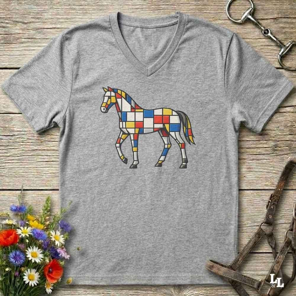 A heather gray V-neck t-shirt featuring a colorful geometric horse graphic in a Mondrian-style pattern, displayed on a rustic wooden background with equestrian-themed props.