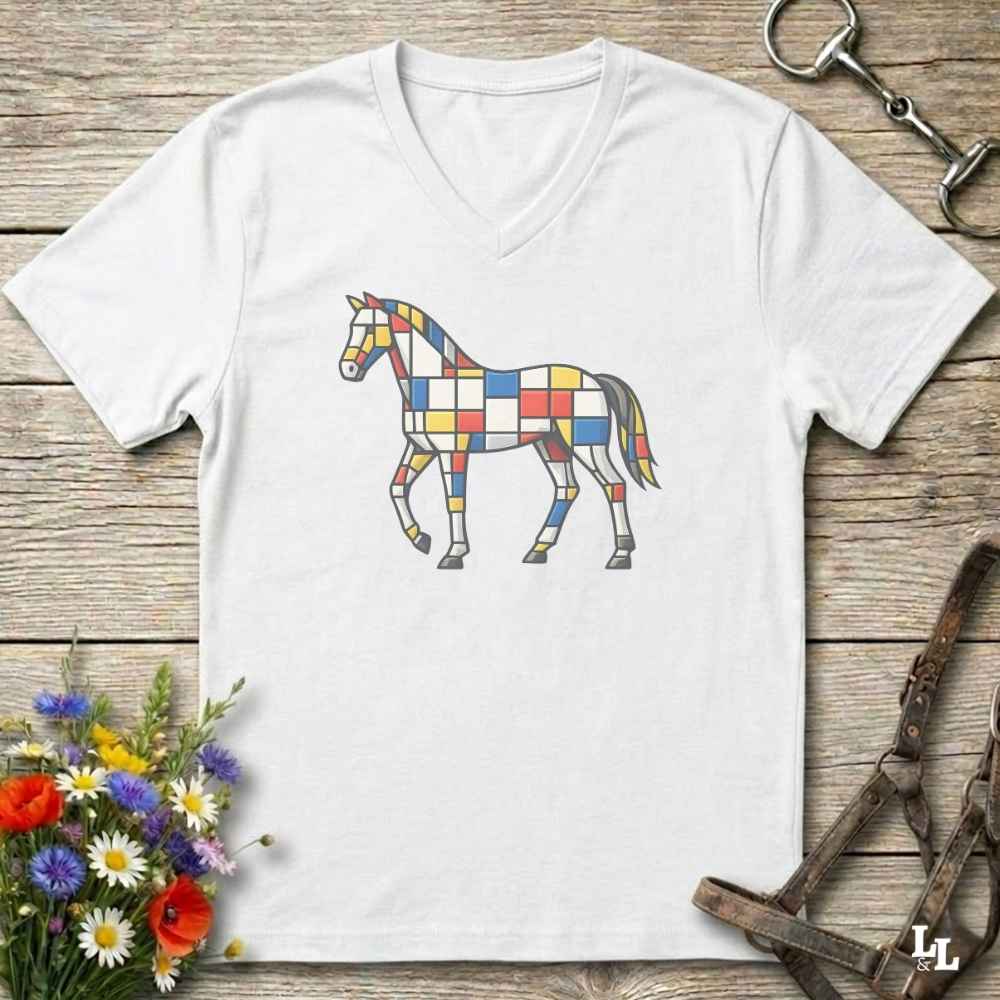 A white V-neck t-shirt laid flat on a rustic wooden surface, featuring a colorful geometric horse graphic on the chest. The shirt is styled with equestrian-themed props, including a horse bit in the top right, a halter in the bottom right, and a small bouquet of wildflowers in the bottom left.