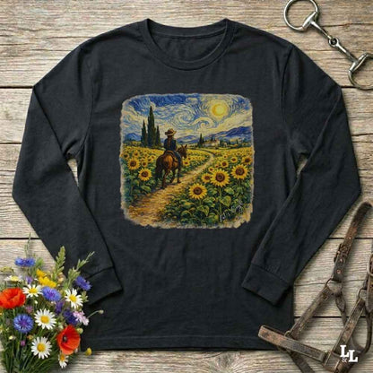 A black long-sleeve t-shirt with a square graphic print of a cowboy riding through a sunflower field in a Van Gogh style, displayed on a rustic wooden background with decorative flowers and horse tack.