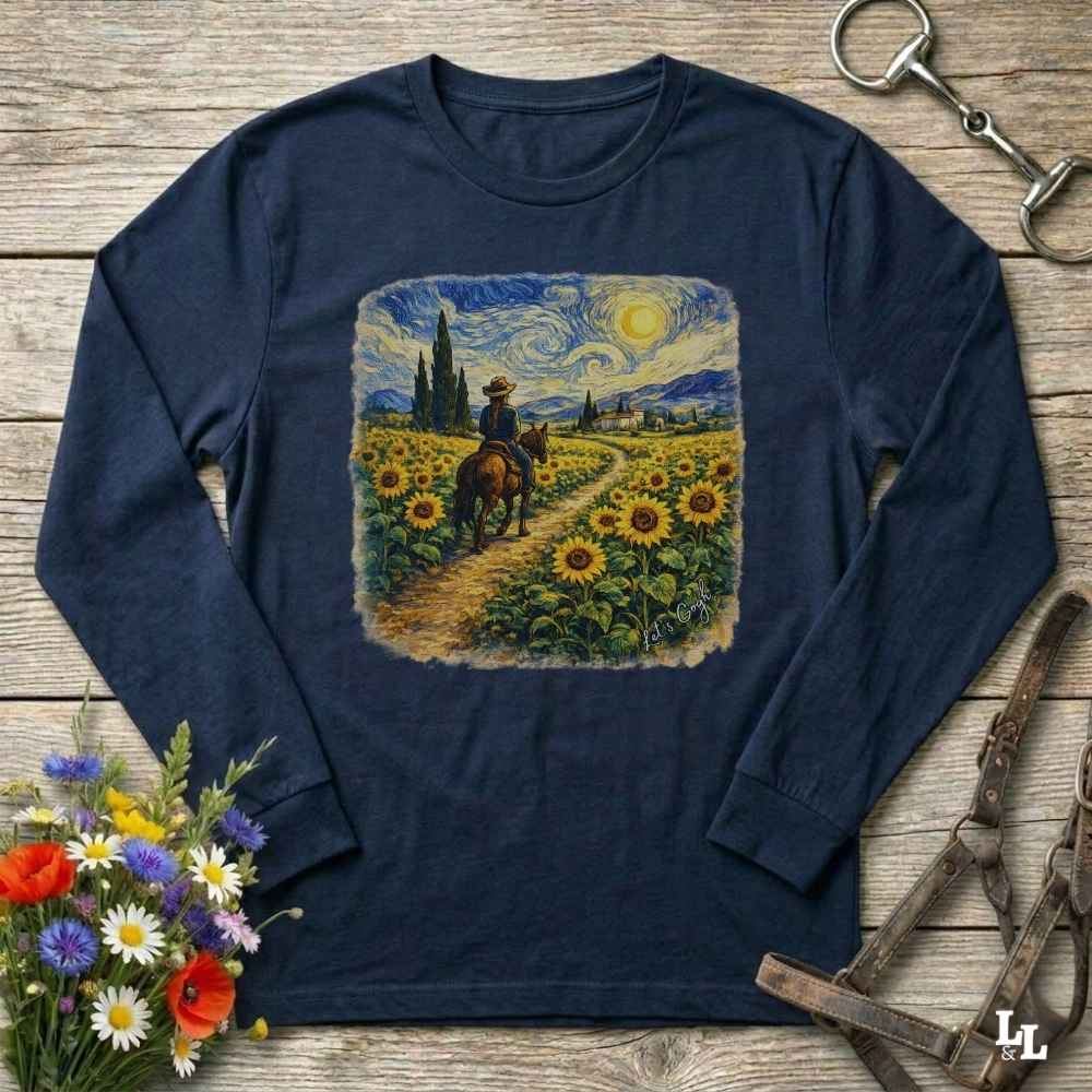 A navy blue long-sleeve t-shirt with a central graphic print of a cowboy riding through a sunflower field in a Van Gogh-inspired style. The shirt is displayed flat on a rustic wooden background with decorative equestrian and floral props.