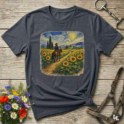 A dark gray heather t-shirt with a square graphic print of a cowboy riding through a sunflower field in a Van Gogh-inspired style. The shirt is displayed flat on a rustic wooden background with equestrian and floral props.