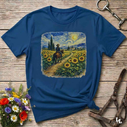 A navy blue short-sleeve t-shirt with a square graphic print of a cowboy riding through a sunflower field in a Van Gogh-inspired style. The shirt is styled in a flat-lay on a rustic wooden background with decorative flowers and leather tack.