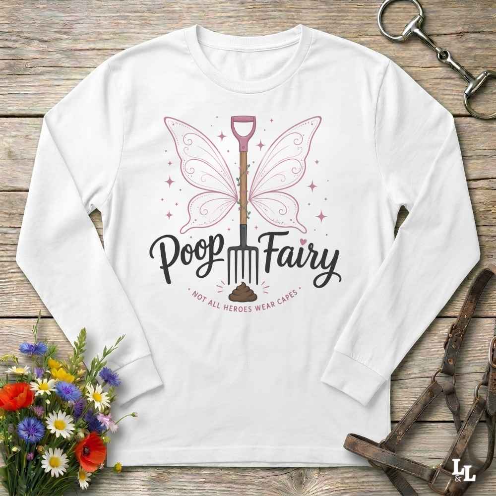 A white long-sleeve t-shirt with a graphic of a butterfly-winged shovel and the text 'Poop Fairy - NOT ALL HEROES WEAR CAPES' in black script, displayed on a rustic wooden background with equestrian accessories and flowers.
