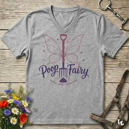 A heather gray V-neck t-shirt with a purple graphic of a butterfly-shaped shovel and the words 'Poop Fairy' on a rustic wooden background, styled with flowers, a horse bit, and a halter.