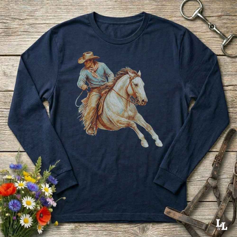 A navy blue long-sleeve t-shirt with a graphic print of a cowboy riding a white horse, laid flat on a rustic wooden background with equestrian and floral props.