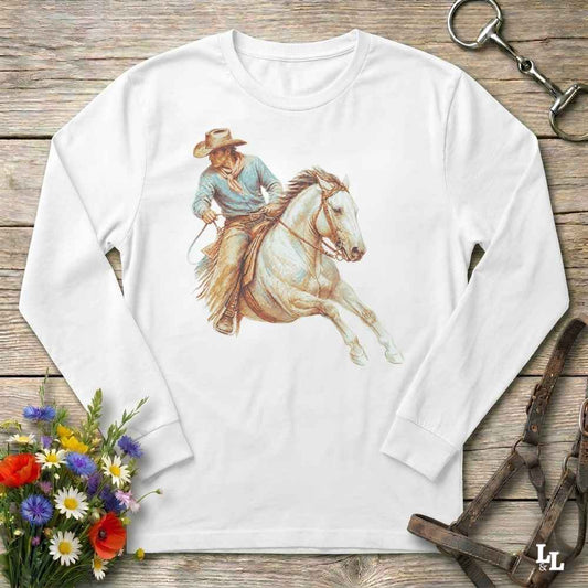 A white long-sleeve t-shirt with a graphic print of a cowboy riding a white horse, laid flat on a rustic wooden background with equestrian accessories and flowers.