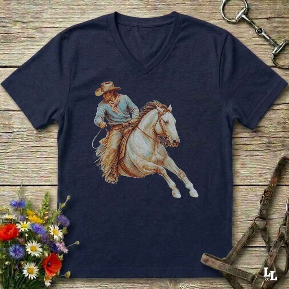 A navy blue V-neck t-shirt featuring a graphic print of a cowboy riding a white horse, laid flat on a rustic wooden background with equestrian accessories and flowers.