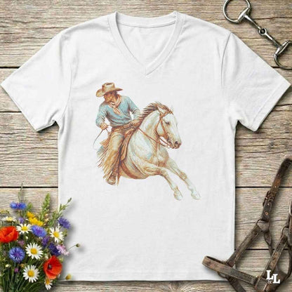 A white V-neck t-shirt laid flat on a rustic wooden surface, featuring a detailed graphic of a cowboy riding a white horse. The shirt is styled with equestrian accessories (a bit and reins) and a small bouquet of colorful wildflowers.