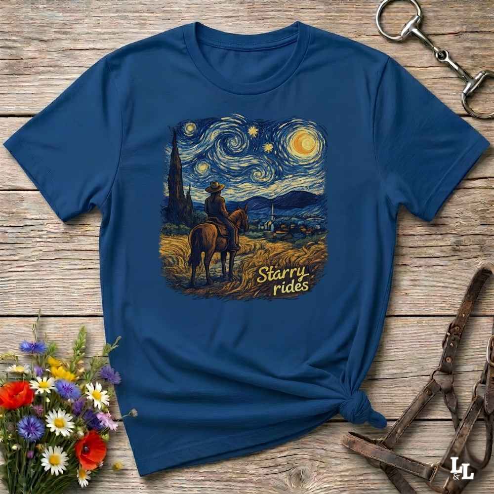 A navy blue short-sleeve t-shirt with a 'Starry Rides' graphic print in a Van Gogh style, styled flat on a rustic wooden background with equestrian accessories and flowers.
