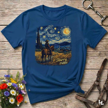A navy blue short-sleeve t-shirt with a 'Starry Rides' graphic print in a Van Gogh style, styled flat on a rustic wooden background with equestrian accessories and flowers.