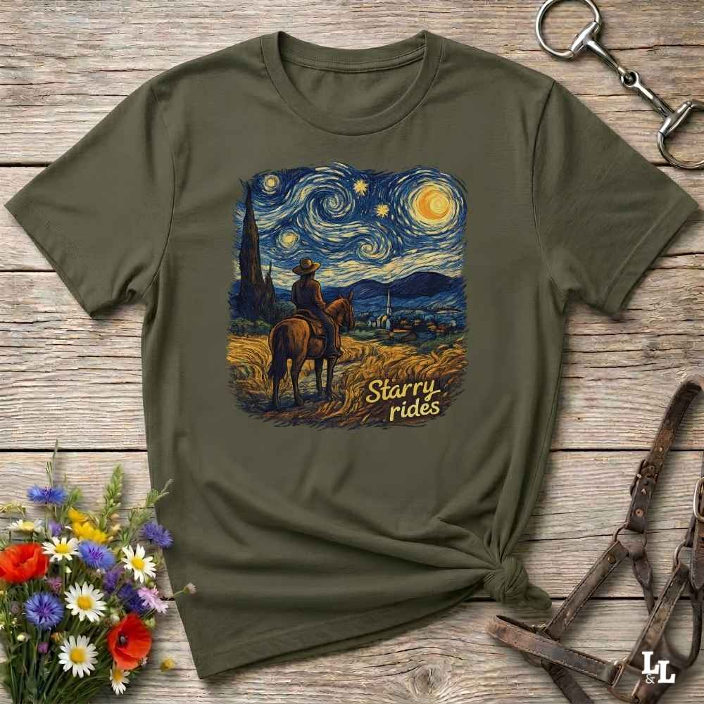An olive green short-sleeve t-shirt with a 'Starry Rides' graphic print, styled in a flat-lay on a rustic wooden background with a horse bit, leather bridle, and wildflowers.