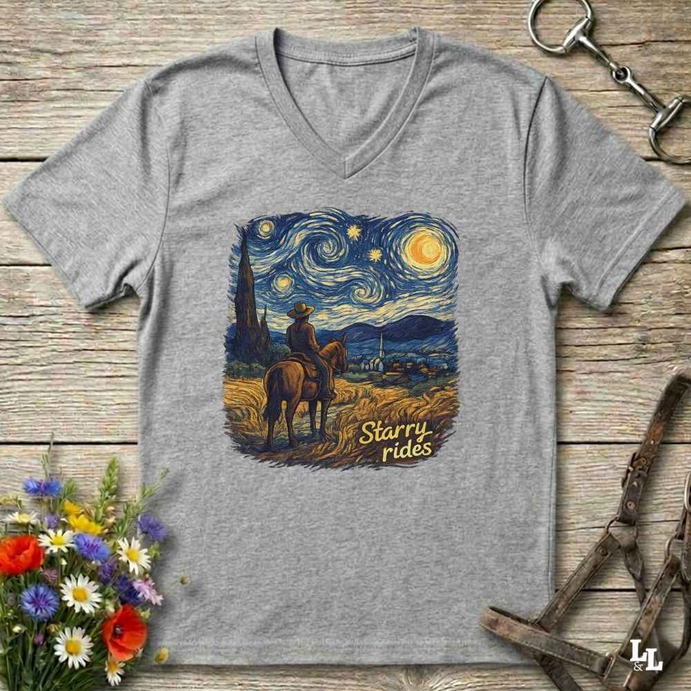 A heather gray V-neck t-shirt laid flat on a rustic wooden surface, featuring a colorful graphic print of a cowboy riding a horse under a swirling 'Starry Night' sky. The text 'Starry rides' is printed in yellow in the lower right of the graphic.