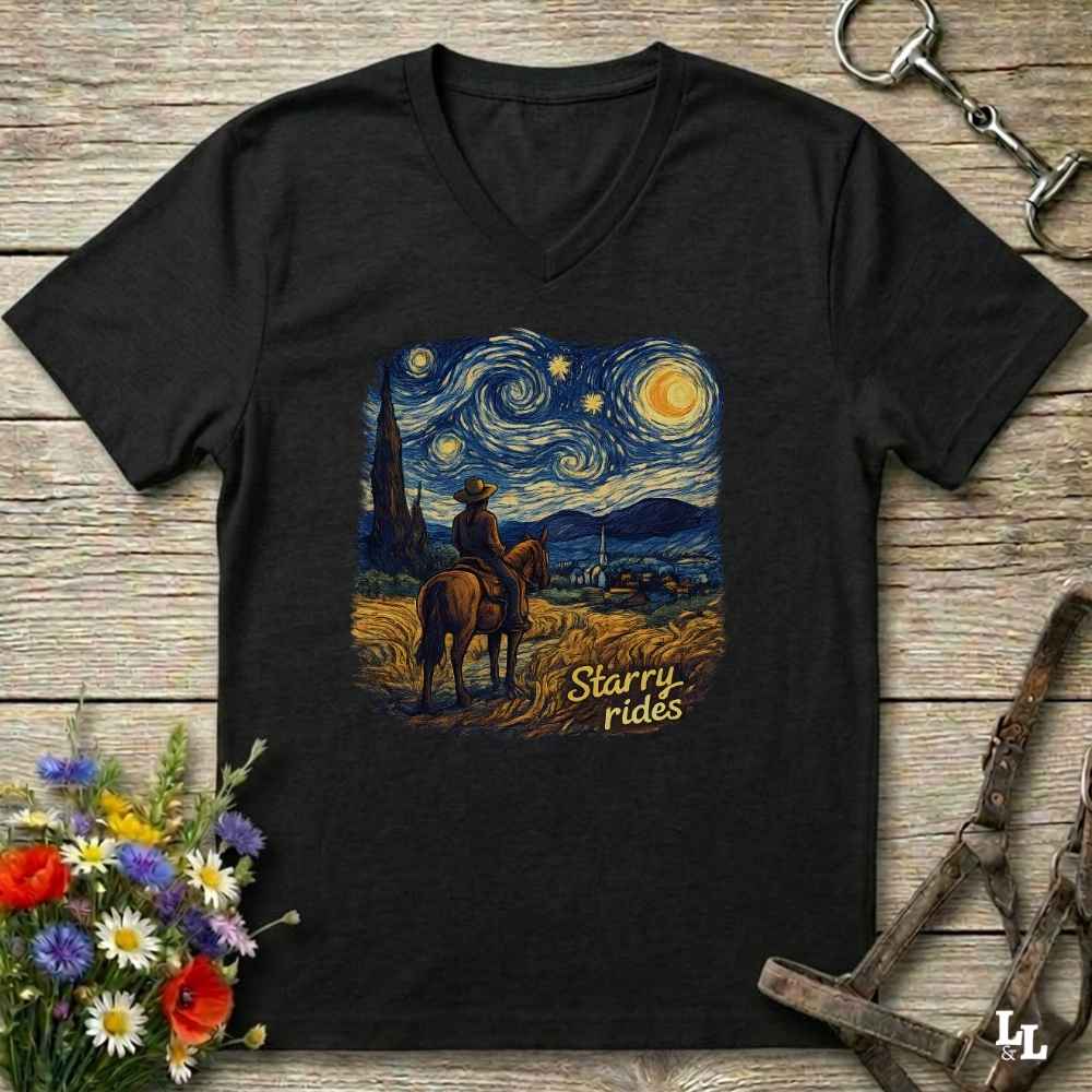 A black V-neck t-shirt laid flat on a rustic wooden surface, featuring a colorful graphic print of a cowboy riding a horse under a swirling Starry Night sky, with the text 'Starry rides'.