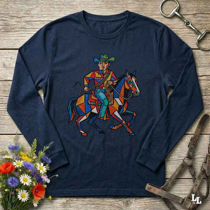 A navy blue long-sleeve t-shirt with a colorful geometric graphic of a cowboy riding a horse, displayed on a rustic wooden background with equestrian and floral props.