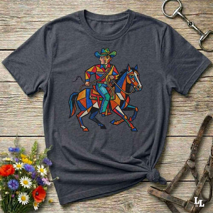 A dark gray heather t-shirt with a colorful graphic of a cowboy riding a horse, styled in a flat-lay on a rustic wooden background with flowers and horse tack.