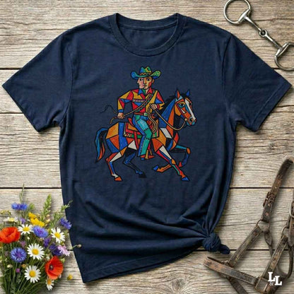 A navy blue short-sleeve t-shirt with a colorful graphic of a cowboy riding a horse, styled on a rustic wooden background with flowers and horse tack.
