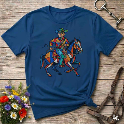 A navy blue short-sleeve t-shirt with a colorful graphic of a cowboy riding a horse, styled on a rustic wooden background with flowers and horse tack.