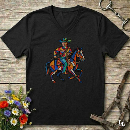 A black V-neck t-shirt featuring a colorful geometric graphic of a cowboy riding a horse, laid flat on a rustic wooden background with decorative flowers and leather tack.