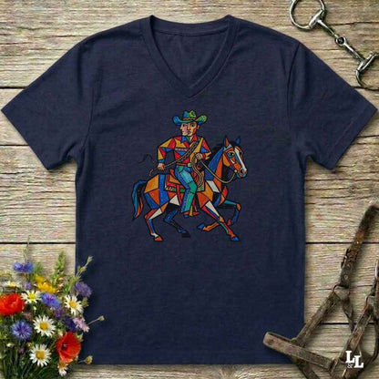 A navy blue V-neck t-shirt laid flat on a rustic wooden surface, featuring a colorful geometric graphic of a cowboy riding a horse. The shirt is styled with equestrian accessories (a bridle and a horse bit) and a small bouquet of wildflowers.