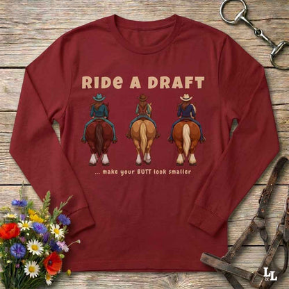 A long-sleeve maroon crewneck t-shirt with a graphic print of three cowboys riding horses from behind, featuring the text 'RIDE A DRAFT .